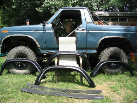 1986 Ford Bronco - Ford Bronco side view with new fender flares laid out on the grass. A child sits in the driver's seat.