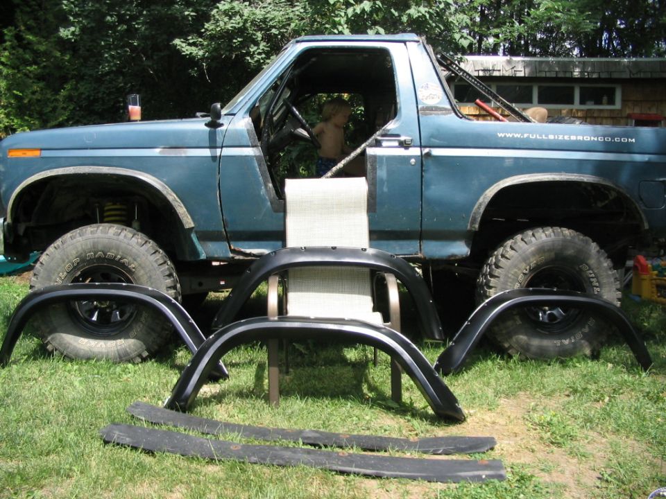 Blue topless Ford Bronco on mud tires with four black fender flares laid out on grass before install