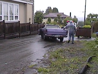 1968 Ford Ranchero - A person stands next to the open tailgate of a purple pickup truck on a wet driveway.