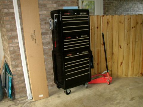 1995 Ford Bronco - A black Craftsman tool chest is parked next to a red floor jack and a long cardboard box, leaning against a brick wall.