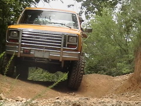 1986 Ford Bronco - This yellow SUV navigates a dirt trail with large, knobby tires.