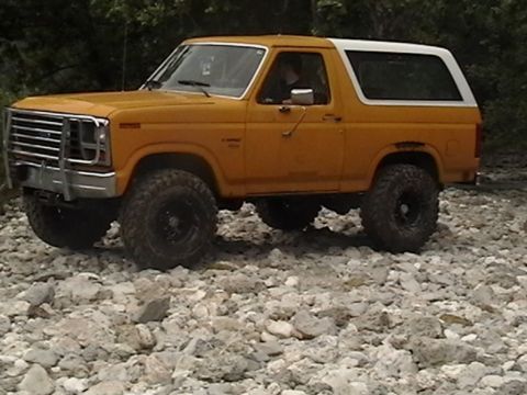 1986 Ford Bronco - This Ford Bronco is navigating a rough, rocky path with trees in the background.