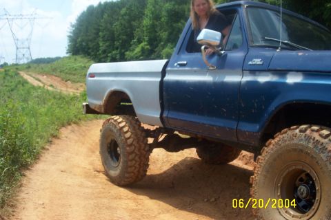 1979 Ford F-150 - A woman sits in the driver's seat of a modified pickup truck on a dirt path with power lines in the background.