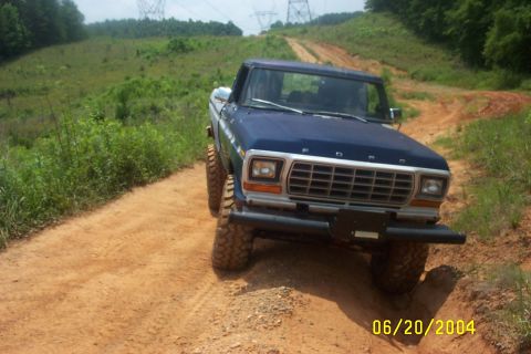1979 Ford F-150 - A blue 1979 Ford F-150 navigates a dusty, off-road trail with power lines visible in the background.