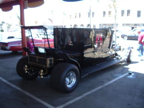 1989 Ford Bronco - A black carriage-style vehicle with oversized rear wheels is parked in a lot.