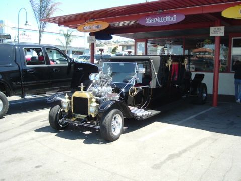 1989 Ford Bronco - A souped-up vintage car with a prominent engine sits in front of a food stand.
