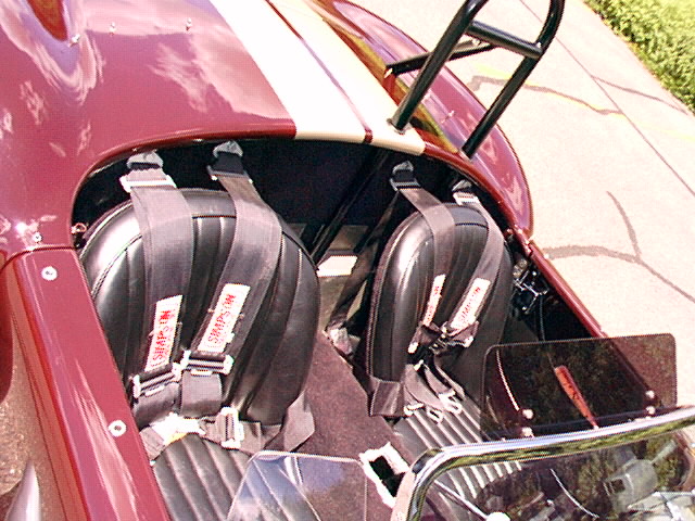 Cockpit of a red roadster with black seats and Simpson racing harnesses