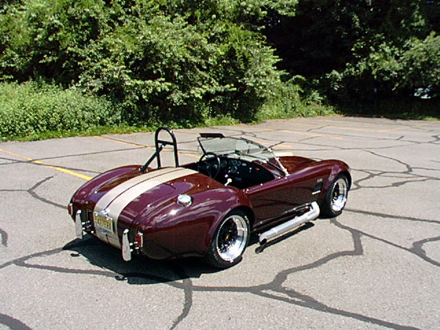 Maroon Cobra roadster with silver stripes, rear 3/4 view on asphalt lot