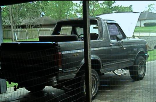 Dark gray Ford Bronco with top removed, rear 3/4 view in a driveway