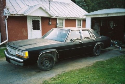 1989 Ford Crown Victoria LTD - A black 1988 Ford Crown Victoria is parked in a driveway next to a house and an open garage.
