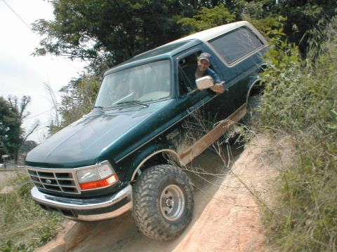 1995 Ford Bronco - A 1995 Ford Bronco navigates an off-road trail, with its tires kicking up dirt on the incline.