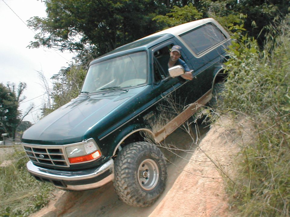 Green 1995 Ford Bronco driving up a dirt hill with a person in the driver's seat