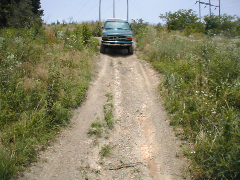 Green SUV driving up a dirt road with power lines in the background