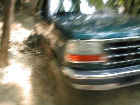 1995 Ford Bronco - A green Ford truck is seen from the front with motion blur, showing its grille and headlight.