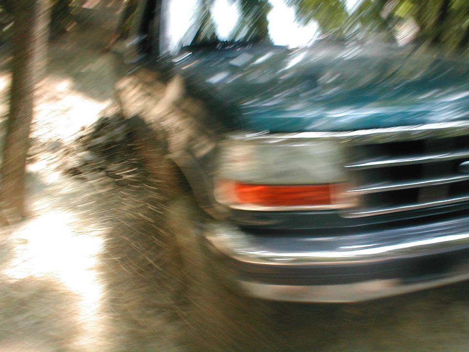 Green Ford truck front end, grille and headlight visible. Motion blur