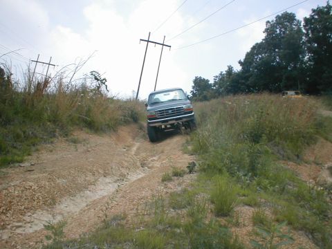1995 Ford Bronco - A 1995 Ford Bronco navigates a rough dirt trail under a cloudy sky.