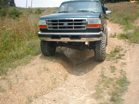 1995 Ford Bronco - A green 1995 Ford Bronco is shown from the front on a dirt path with vegetation on the sides.