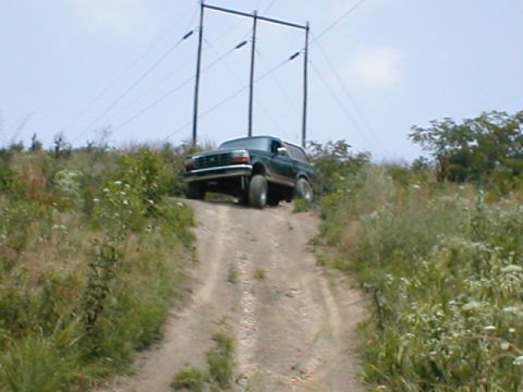 1995 Ford Bronco - A dark green 1992 Ford Bronco navigates an off-road dirt path under a clear sky.
