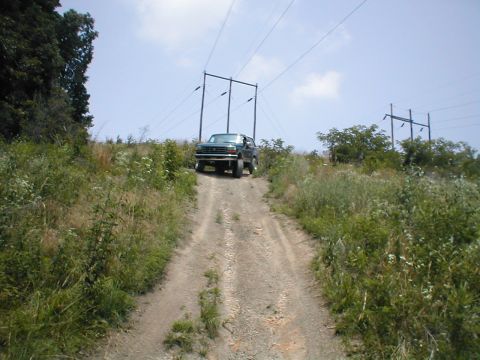 1995 Ford Bronco - A dark green 1995 Ford Bronco ascends a dirt path under power lines.