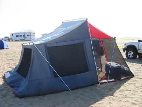 1985 Ford Bronco - A large tent is set up on a beach, with a white SUV and an RV visible in the distance.