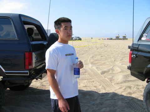 1985 Ford Bronco - A person stands by a black Ford Bronco on a sandy beach with other vehicles in the background.