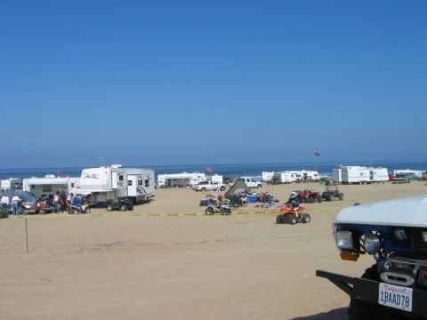 1985 Ford Bronco - A busy beach scene with multiple RVs and ATVs parked on the sand near the ocean.