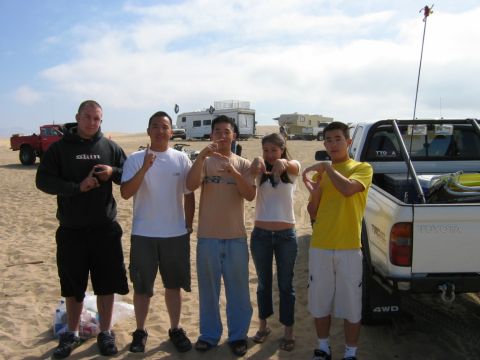 1985 Ford Bronco - A group of friends pose with vehicles in a sandy outdoor setting, possibly a desert or beach.