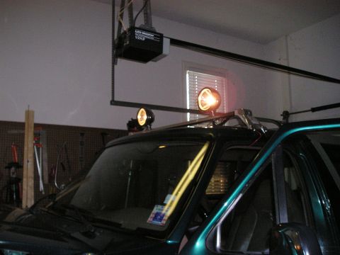 1996 Ford Bronco - Spotlights are mounted on the roof rack of a dark green SUV in a garage.