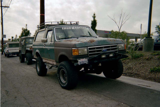 Weathered teal-and-brown Ford Bronco with roof rack labeled FOUR X DOOR