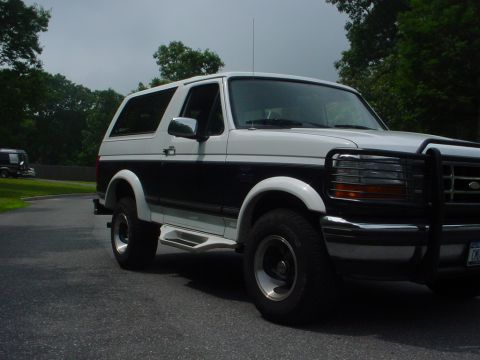 1995 Ford Bronco - A two-door Ford Bronco is parked on a paved surface with trees in the background.