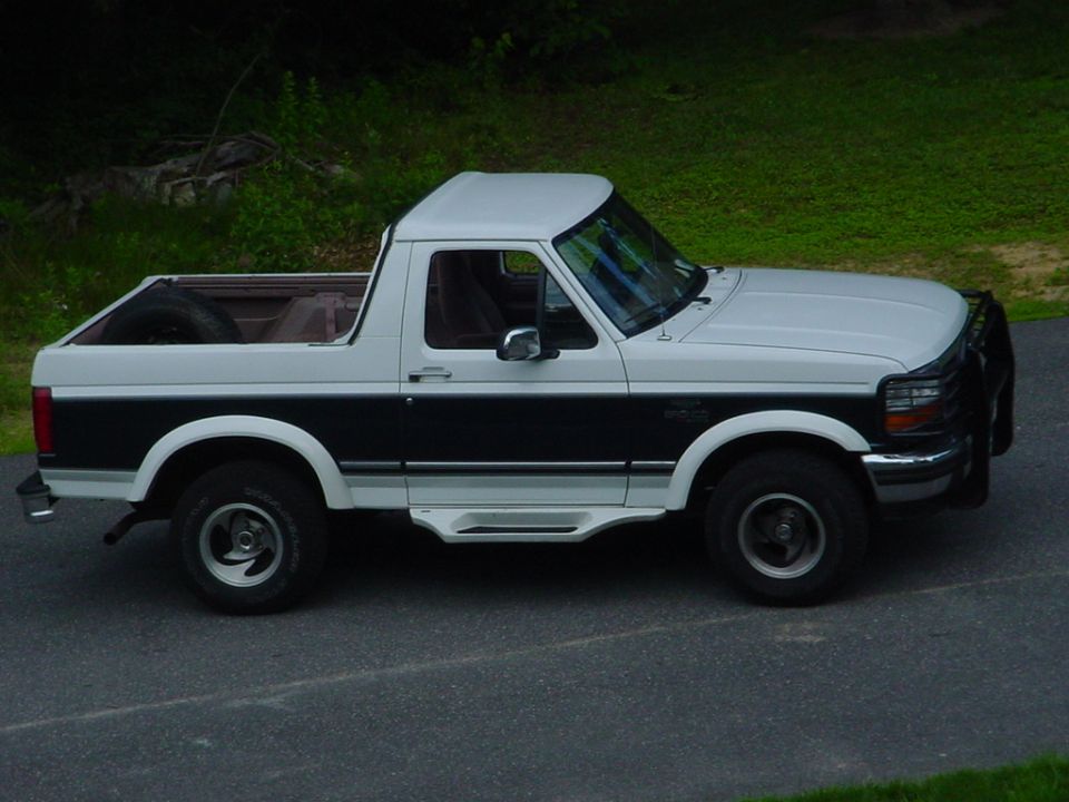 Two-tone white and dark green Ford Bronco, top removed, side view on driveway