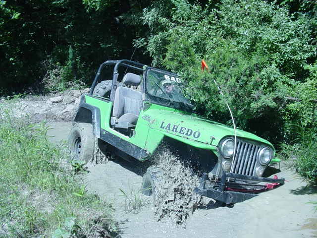 Green Jeep Wrangler with 'LAREDO' text on the side driving through mud