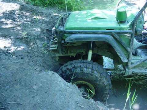 1992 Ford Bronco - Off-road vehicle is deeply stuck in mud, with one wheel submerged in water.