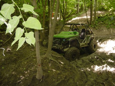 1992 Ford Bronco - This modified off-road vehicle tackles a challenging muddy path in a wooded area.
