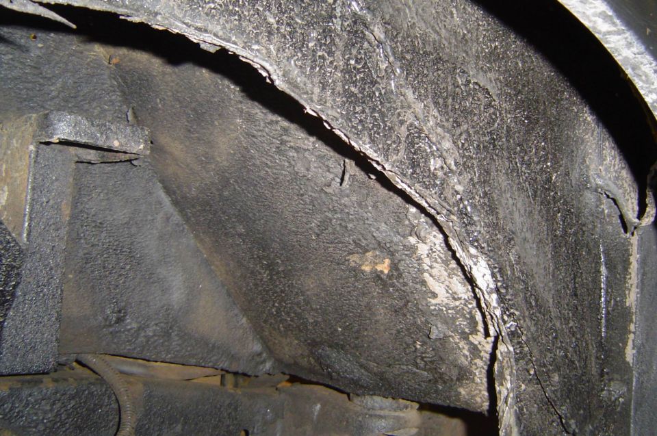 Rusted torn inner fender lip inside a wheel well with flaking undercoating