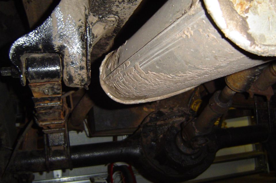 Underside view of a vehicle's exhaust pipe, muffler, leaf spring, and rear axle assembly