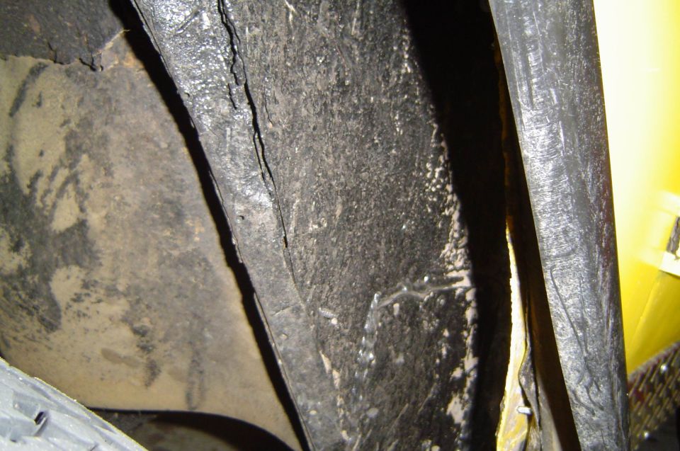 Close-up of cracked black undercoated body panel next to a yellow panel, covered in grime