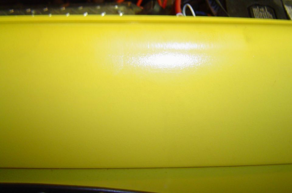 Close-up of glossy yellow painted vehicle body panel in workshop