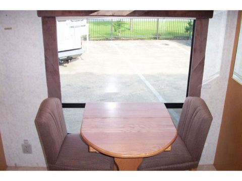 1989 Ford C-350 (Centurion Conversions) - The interior of a recreational vehicle shows a dining nook with a table and chairs, looking out at a parking lot and a white camper.