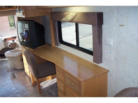1989 Ford C-350 (Centurion Conversions) - The interior of a motorhome features a built-in desk with drawers and a chair, next to a television.