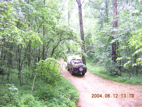 1984 Chevrolet Blazer - A dark SUV navigates a wooded path, its spare tire visible on the back.