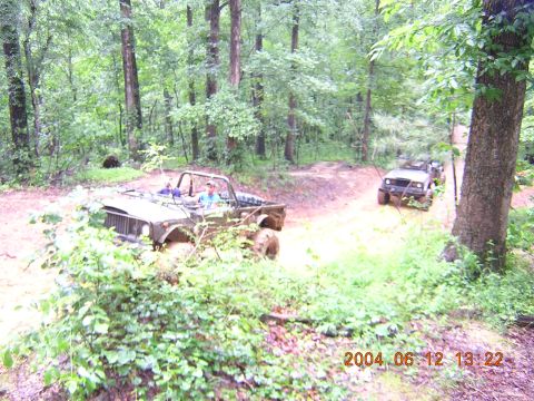 1984 Chevrolet Blazer - Two off-road vehicles are seen driving through a muddy forest trail, with one vehicle in the foreground and another further down the path.