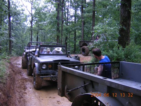 1984 Chevrolet Blazer - Several military-style off-road vehicles navigate a muddy path through a dense forest.