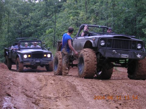 1984 Chevrolet Blazer - Two off-road vehicles navigate a muddy path through a wooded area.