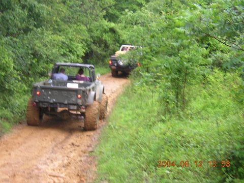 1984 Chevrolet Blazer - Several off-road vehicles navigate a muddy trail surrounded by lush green foliage.
