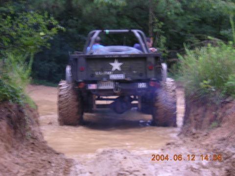 1984 Chevrolet Blazer - This army truck navigates a muddy trail with its large tires kicking up water.