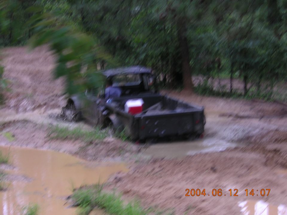 Dark colored pickup truck stuck in muddy terrain, red and white cooler in bed