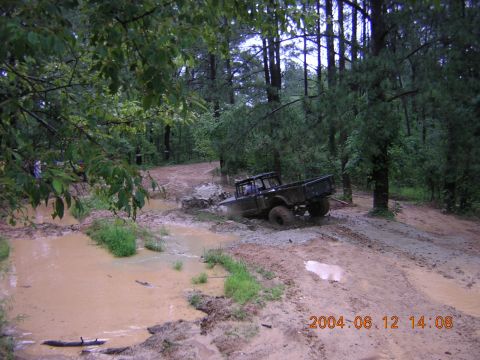 1984 Chevrolet Blazer - A dark-colored off-road truck navigates a muddy trail through a wooded area.