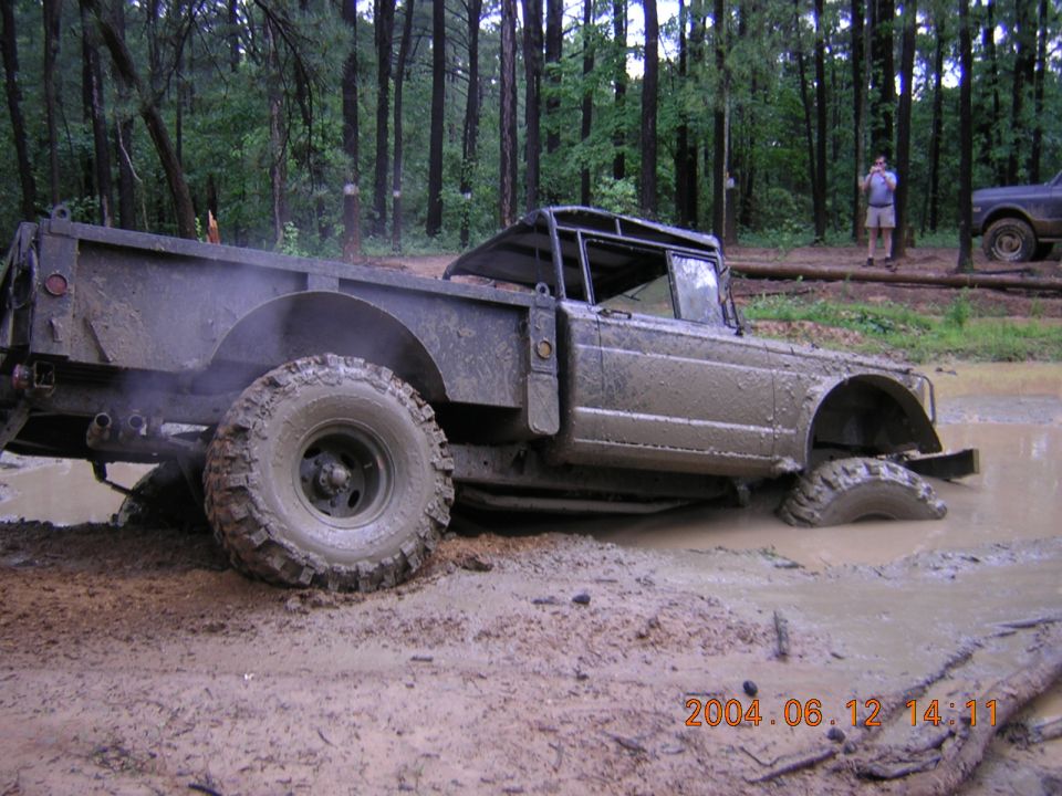 Muddy off-road truck stuck in a mud pit with trees in background. Another vehicle visible to the right