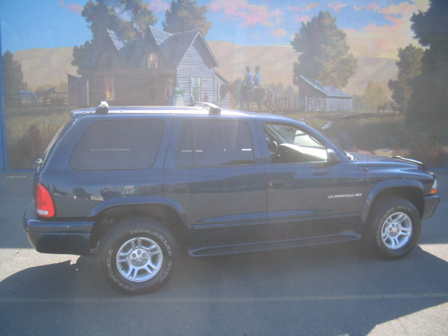 Dark blue Dodge Durango SUV in side profile parked before a rustic mural
